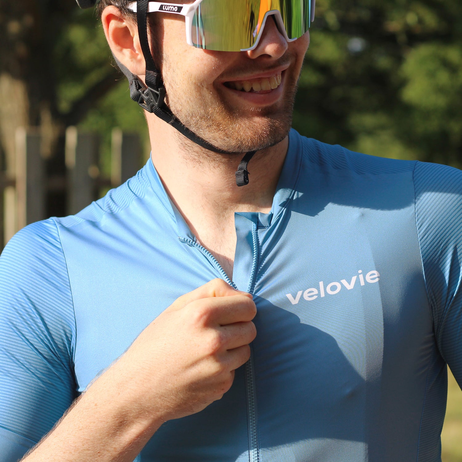 Man wearing a blue cycling jersey with 'velovie' branding, smiling outdoors.