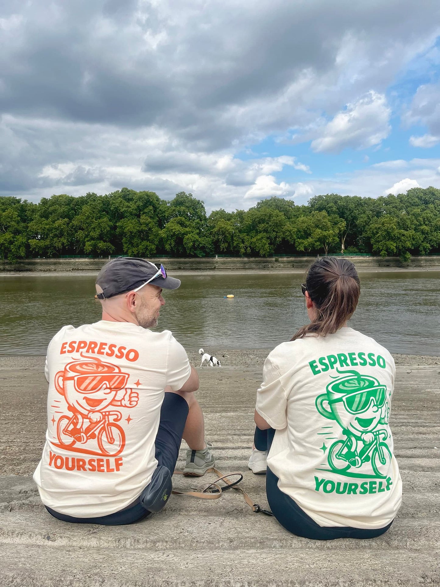 Two people sitting by a lake wearing t-shirts with 'Espresso Yourself' text and graphics.